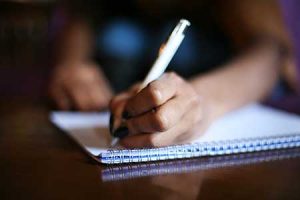 hand holding a pen and writing on a pad of paper