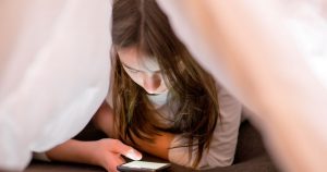 Young girl looking at iphone under her covers