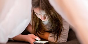 Young girl looking at iphone under her covers